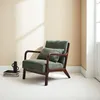 A green corduroy armchair with a wooden frame is placed on a white floor against a cream-colored wall. Sunlight casts shadows on the wall. Produktbild-Vorschau