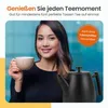 A woman is holding a cup and a black kettle is beside her. Produktbild-Vorschau