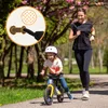 A woman runs alongside a young child on a balance bike in a park. Produktbild-Vorschau