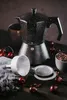 A speckled black moka pot with coffee beans, cherries, and a coffee filter on a wooden surface. Náhľad obrázku produktu