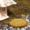 A bird is eating seeds from a wooden bowl next to a birdhouse. Produktbild-Vorschau