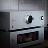 Two silver audio components are stacked on top of each other, with the top component being a network pre-amplifier and the bottom component appearing to be an amplifier. Produktbild-Vorschau