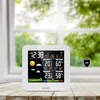 A white weather station is placed on a wooden table in front of a window with greenery outside. Náhled obrázku produktu