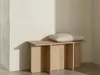 A modern wooden bench with a fluffy pillow on top, placed against a light-colored wall with soft shadows. Produktbild-Vorschau