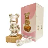 A silver bear-shaped night light with a wooden base, placed next to its pink and white packaging. A white USB cable is also visible. Voir les images du produit