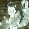 A close-up shot of a decorative angel figure made of wire and lights, set against a stone wall. Náhled obrázku produktu