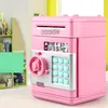 A pink electronic piggy bank with a keypad and a coin slot is shown in a room with shelves in the background. Náhľad obrázku produktu
