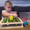 A young boy is playing with a wooden toy garden set on a table. Voir les images du produit