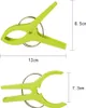 Two green plastic clothes pegs with metal springs are shown with dimensions indicated by lines and text. Produktbild-Vorschau
