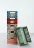 A stack of colorful, foldable storage crates with one crate open and leaning against the stack. Produktbild-Vorschau