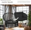 A black macrame hanging chair with tassels is shown in a living room setting, with an arrow pointing to a separate black cushion. Náhled obrázku produktu