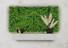 A decorative green plant wall with a shelf below, featuring a lamp, a vase with dried flowers, and a small bowl. Produktbild-Vorschau