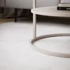 A close-up of a modern coffee table with a round base and a shelf, placed on a light-colored rug. Náhľad obrázku produktu