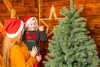 A woman holding a child in front of a Christmas tree and wooden wall. Produktbild-Vorschau