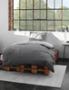 A bedroom scene with a bed made of wooden pallets, a grey duvet, and a large window. Produktbild-Vorschau