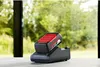 A battery charger with a battery inserted, placed on a table in front of a window with greenery outside. Produktbild-Vorschau