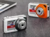 Two mini digital cameras are placed on a textured gray surface, with a notebook partially visible in the background. Produktbild-Vorschau
