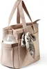 A close-up view of a beige diaper bag with a bottle in a side pocket and a scarf tied to the handle. Produktbild-Vorschau