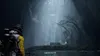 A character in a yellow suit stands in a dark, misty forest with ancient ruins. Produktbild-Vorschau