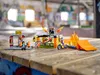 A LEGO stunt park set with a motorcycle and figures is displayed on a wooden surface, with a blurred background of a skatepark. Podgląd zdjęcia produktu