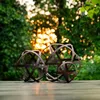 Three metal garden spheres of varying sizes are placed on a wooden deck in a garden setting with blurred green foliage and bokeh lights in the background. Voir les images du produit