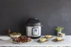An Instant Pot Duo Crisp Multikocher is displayed on a counter with prepared meals, suggesting its versatility in cooking. Produktbild-Vorschau
