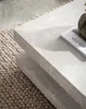 A close-up of a modern, square coffee table with a stone-like texture, placed on a textured rug. Produktbild-Vorschau