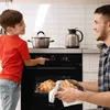 A father and son are in a kitchen, with the son operating the oven controls while the father holds a tray of freshly baked croissants. Náhled obrázku produktu