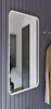 A mirror with a white frame is mounted on a grey slatted wall. Produktbild-Vorschau