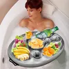A woman relaxing in a bubble bath with a tray of drinks and snacks floating on the water. Náhled obrázku produktu