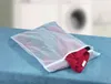 A mesh laundry bag filled with clothes sits on a blue towel, with a blurred background of laundry machines. Anteprima dell’immagine prodotto