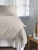 A close-up view of a bed with natural-colored bedding, set against a window with natural light. Produktbild-Vorschau