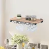 A wooden shelf with a wine glass rack mounted underneath, holding several wine glasses. There are also jars and a small plant on the shelf. The shelf is mounted on a wall above a dining table with a floral arrangement. Voir les images du produit