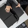 A person is placing a black laptop into a black laptop bag. Produktbild-Vorschau