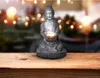 A Buddha statue holding a bowl with a light inside, placed on a wooden surface with a blurred background of lights. Anteprima dell’immagine prodotto