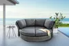 A round outdoor daybed with gray cushions is placed on a wooden deck next to a swimming pool with the ocean in the background. Produktbild-Vorschau