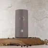 A taupe electric coffee grinder with gold accents sits on a piece of wood, surrounded by coffee beans and dried flowers, against a marble-like background. Náhľad obrázku produktu