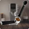 A close-up shot of an espresso machine's portafilter filled with coffee grounds, with a coffee tamper hovering above it, indicating a step in the coffee-making process. The background shows a blurred espresso machine and a wooden surface. Anteprima dell’immagine prodotto