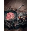 A raw steak is being seared in a cast iron pan over an open fire. Produktbild-Vorschau