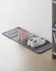 A shoe drying mat with pink boots and white sneakers on it, placed against a white wall and baseboard. Náhled obrázku produktu