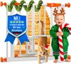 A baby in a Christmas sweater and reindeer antlers holds a candy cane next to a white safety gate decorated with Christmas garland. An orange cat wearing a Santa hat is hanging upside down from the gate. The background shows wooden stairs. Produktbild-Vorschau