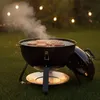 A charcoal grill with burgers cooking on it, set up in a grassy backyard at dusk with string lights in the background. Produktbild-Vorschau