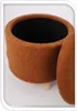 A close-up view of a round, upholstered storage ottoman with a textured brown fabric and wooden legs. Produktbild-Vorschau