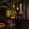 Three oil lamps made from recycled bottles are displayed on a dark surface, with a potted plant in the background. Produktbild-Vorschau