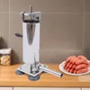 A stainless steel sausage stuffer is shown on a wooden countertop, with a plate of sausages in the foreground. Náhled obrázku produktu