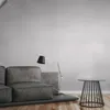 A modern living room setting with a grey sofa, a floor lamp, and a small side table. Podgląd zdjęcia produktu