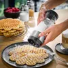 A person is dusting powdered sugar onto waffles using a powder sugar mill. Podgląd zdjęcia produktu