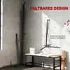A black foldable boxing stand is shown in a corner of a room with a concrete wall. There is a table with towels and a yoga mat nearby. Produktbild-Vorschau