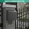 A black mailbox mounted on a stone pillar next to a black metal fence. Produktbild-Vorschau