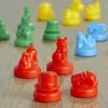 A close-up shot of various colorful Monopoly game pieces arranged on a wooden surface. Voir les images du produit